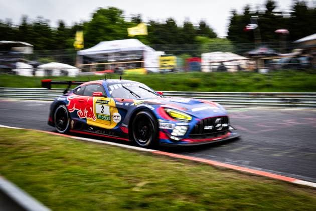 Der Mercedes-AMG GT3 mit der Startnummer 3 von Mercedes-AMG Team Verstappen Racing durchfährt mit hoher Geschwindigkeit eine Kurve auf dem Nürburgring. Das Fahrzeug trägt das markante Red Bull-Livery in Blau, Rot und Gelb mit RAVENOL- und DEKRA-Sponsoring. Die Panning-Aufnahme betont die Dynamik des Rennwagens, während der Hintergrund mit Boxenanlagen und Bäumen verschwimmt. Daniel Juncadella & Jules Gounon & Lucas Auer & Max Verstappen (Mercedes-AMG Team Verstappen Racing) Mercedes-AMG GT3 3 von Verstappen Racing auf dem Nürburgring Copyright: xMichaelxGelhardtx
