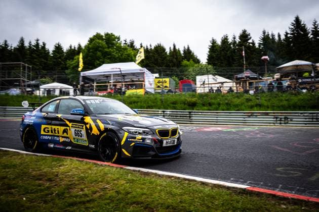 Der BMW M235i Racing 665; LG Bamberg von GITI TIRE MOTORSPORT BY WS RACING durchfährt eine Kurve auf der Nordschleife am Nürburgring. Das Fahrzeug trägt das markante schwarz-gelbe Giti-Livery mit auffälligen Camouflage-Mustern. Deutlich sichtbare Sponsoren sind Giti Competition Tires, RAVENOL und DEKRA. Im Hintergrund sind Zuschauer, Zelte und die charakteristische grüne Vegetation der Eifel zu sehen. BMW M235i Racing 665 von GITI TIRE MOTORSPORT BY WS RACING auf der Nordschleife Copyright: xMichaelxGelhardtx
