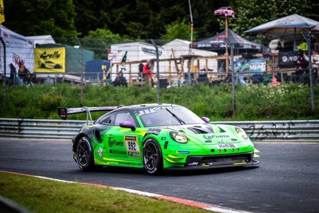 Der Porsche 911 GT3 R Björn Griesemann & Dirk Adorf & Georg Griesemann & Marco Holzer (Manthey Team eFuel Griesemann) von Manthey Team eFuel Griesemann durchfährt eine Kurve auf der Nordschleife des Nürburgrings. Das Fahrzeug trägt das markante neongrüne Livery mit eFuels- und RAVENOL-Sponsoring und ist mit der Startnummer 992 versehen. Im Hintergrund sind Zuschauer, Fanzelte und das typische Ambiente des 24h-Rennens zu sehen. Porsche 911 GT3 R 992 von Manthey Team eFuel Griesemann auf der Nordschleife Copyright: xMichaelxGelhardtx