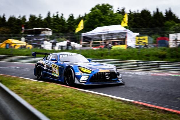 Der Andreas Gülden & Tim Sandtler & Yuichi Nakayama (Toyo Tires with Ring Racing) Mercedes-AMG GT3 von Toyo Tires with Ring Racing durchfährt dynamisch eine Kurve auf dem Nürburgring. Das blau-goldene Fahrzeug mit der Startnummer 32 und markanten gelben Scheinwerfern ist in leichter Bewegungsunschärfe festgehalten, was die hohe Geschwindigkeit unterstreicht. Im Hintergrund sind Zuschauerbereich und Sponsorenzelte des 24h-Rennens zu sehen. Mercedes-AMG GT3 32 von Toyo Tires with Ring Racing auf dem Nürburgring Copyright: xMichaelxGelhardtx