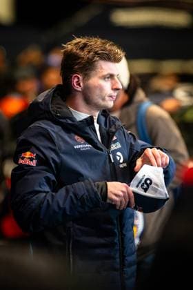 Max Verstappen steht im Fahrerlager des Nürburgrings in der dunkelblauen Teamjacke von Verstappen Racing mit Red-Bull-Logo und hält eine weiße Cap in den Händen. Im Hintergrund sind weitere Personen und die typische Paddock-Atmosphäre zu erkennen. Max Verstappen im Fahrerlager beim 24h Nürburgring 2026 Copyright: xMichaelxGelhardtx