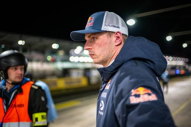 Max Verstappen steht konzentriert in der beleuchteten Boxengasse des Nürburgrings. Er trägt eine Red Bull-Kappe mit AlphaTauri-Schriftzug sowie eine dunkelblaue Red Bull-Jacke mit Viaplay- und SOTO-Sponsoren. Im Hintergrund ist ein Streckenposten in orangefarbener Warnweste erkennbar. Die nächtliche Atmosphäre der Boxengasse ist durch die helle Hallenbeleuchtung geprägt. Max Verstappen in der Boxengasse beim 24h Nürburgring 2026 Copyright: xMichaelxGelhardtx