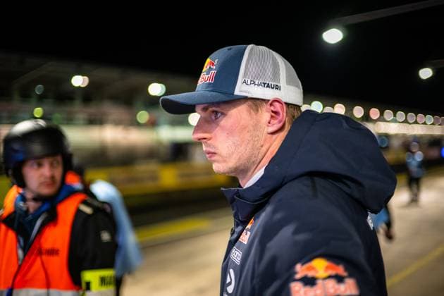 Max Verstappen (3_Driver) steht konzentriert im Fahrerlager des Nürburgrings. Er trägt eine Red Bull AlphaTauri Cap sowie eine dunkelblaue Red Bull Jacke mit Sog und weiteren Sponsoren-Logos. Im Hintergrund ist ein Streckenposten in orangefarbener Warnweste erkennbar, die beleuchtete Boxengasse und Tribünenlichter sind unscharf im Hintergrund zu sehen. Max Verstappen im Fahrerlager am Nürburgring bei Nacht Copyright: xMichaelxGelhardtx