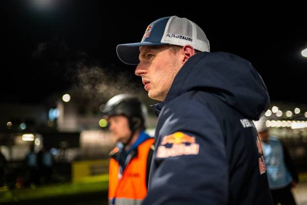 Max Verstappen vom Mercedes-AMG Team Verstappen Racing steht bei Nacht im Fahrerlager des Nürburgrings. Er trägt eine AlphaTauri-Cap sowie eine dunkelblaue Red Bull-Jacke und blickt konzentriert zur Seite. Im Hintergrund ist eine weitere Person mit Helm und orangefarbener Weste zu erkennen, die Boxengassen-Atmosphäre ist stimmungsvoll beleuchtet. Max Verstappen im Fahrerlager beim 24h Nürburgring 2026 Copyright: xMichaelxGelhardtx