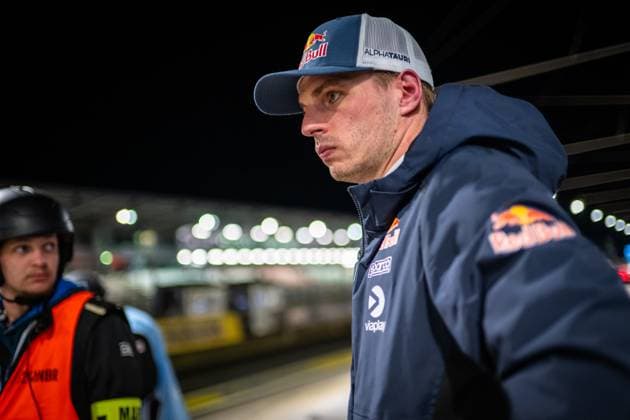 Max Verstappen vom Mercedes-AMG Team Verstappen Racing steht konzentriert in der Boxengasse am Nürburgring. Er trägt eine Red Bull AlphaTauri Cap sowie eine dunkelblaue Jacke mit Red Bull- und Viaplay-Logo. Im Hintergrund sind die beleuchteten Boxenanlagen und ein Streckenposten in orangefarbener Weste zu erkennen. Max Verstappen im Fahrerlager beim 24h Nürburgring 2026 Copyright: xMichaelxGelhardtx