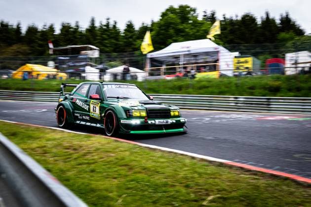 Der dunkelgrüne Mercedes-Benz Rennwagen mit der Startnummer 63 von HWA Engineering Speed durchfährt dynamisch eine Kurve auf dem Nürburgring. Das Fahrzeug trägt auffällige Sponsoren-Logos wie PARKSIDE und RAVENOL und ist mit gelb getönten Scheinwerfern sowie einem markanten Heckflügel ausgestattet. Die Aufnahme wurde mit Panning-Technik erstellt, wodurch der Hintergrund mit den gelben RAVENOL-Fahnen und dem Fahrerlager-Bereich im Unschärfe-Bokeh verschwimmt. Adam Adelson & James Green & Lance David Arnold & Renger Van der Zande (HWA Engineering Speed) Mercedes-Benz 63 von HWA Engineering Speed auf dem Nürburgring Copyright: xMichaelxGelhardtx