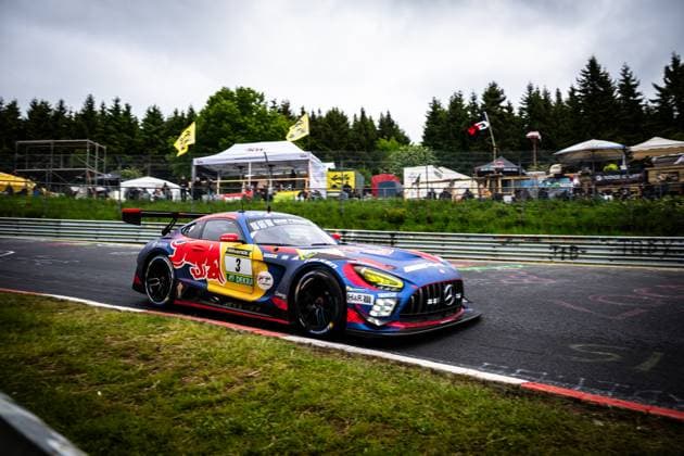 Der Mercedes-AMG GT3 Daniel Juncadella & Jules Gounon & Lucas Auer & Max Verstappen (Mercedes-AMG Team Verstappen Racing) von Mercedes-AMG Team Verstappen Racing durchfährt eine schnelle Kurve auf der Nürburgring-Nordschleife. Das Fahrzeug trägt das charakteristische Red-Bull-Livery in Blau, Rot und Gelb mit RAVENOL- und DEKRA-Sponsoring. Im Hintergrund sind Zuschauer, Zelte und gelbe Fahnen des 24h-Rennens zu sehen. Mercedes-AMG GT3 3 von Verstappen Racing auf der Nordschleife Copyright: xMichaelxGelhardtx