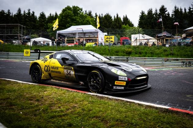 Der Christian Krognes & Mattia Drudi & Nicki Thiim & Felipe Fernandez Laser (natural elements by Walkenhorst Motorsport) von natural elements by Walkenhorst Motorsport durchfährt eine Kurve auf der Nordschleife des Nürburgrings. Das schwarz-gelbe Fahrzeug trägt die Startnummer 34 und ist mit Sponsoren wie RAVENOL und Pirelli-Reifen ausgestattet. Im Hintergrund sind Zuschauer und Zelte des Fahrerlagers zu sehen, während das nasse Wetter die Strecke fordernd macht. Aston Martin GT3 34 von natural elements by Walkenhorst Motorsport am Nürburgring Copyright: xMichaelxGelhardtx