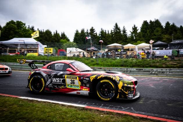 Der BMW Z4 GT3 Christian Scherer & Henry Walkenhorst & Julian Reeh & Ralf Schall (Saugmotoren Motorsport 3M) von Saugmotoren Motorsport 3M nimmt eine Kurve auf der Nordschleife des Nürburgrings. Das Fahrzeug trägt ein markantes schwarz-rot-gelbes Camouflage-Livery mit den Sponsoren W.S.T. (Welding Specialists Team), RAVENOL, DEKRA und 3M. Im Hintergrund sind Zuschauer, Zelte und Bäume zu sehen, die typische Atmosphäre des 24h Nürburgring-Events. BMW Z4 GT3 36 von Saugmotoren Motorsport 3M auf der Nordschleife Copyright: xMichaelxGelhardtx