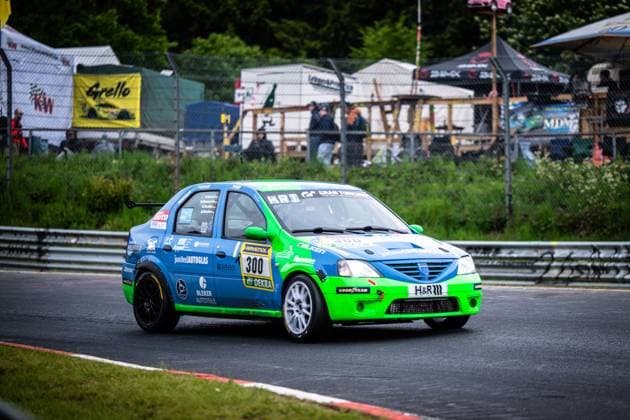 Der Dacia Logan Christian Geilfus (JS Competition) von JS Competition absolviert eine Runde auf dem Nürburgring beim ADAC RAVENOL 24h Nürburgring 2026. Das auffällig in Blau und Neongrün lackierte Fahrzeug trägt die Startnummer 300 und ist mit Sponsoren wie RAVENOL, Falken, GoodYear, H&R und Bleker Autoteile versehen. Im Hintergrund sind die typischen Zuschauerbereiche der Nordschleife mit Fanzonen und Bannern zu sehen. Dacia Logan 300 von JS Competition auf dem Nürburgring Copyright: xMichaelxGelhardtx