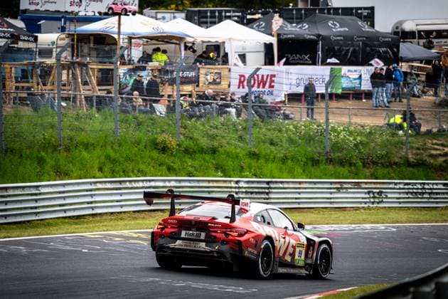 Der Dan Harper & Dries Vanthoor & Max Hesse & Sheldon van der Linde (ROWE RACING) BMW M4 GT3 von ROWE RACING durchfährt eine schnelle Kurve auf dem Nürburgring beim ADAC RAVENOL 24h Nürburgring 2026. Das rot-schwarz lackierte Fahrzeug mit der Startnummer 99 und prominentem ROWE-Sponsoring ist von hinten zu sehen, der große Heckflügel und der MCG-Schriftzug auf dem Heck sind deutlich erkennbar. Im Hintergrund säumen zahlreiche Zuschauer die mit Werbebannern von ROWE Motor Oil und Grünbeck geschmückte Strecke. BMW M4 GT3 99 von ROWE RACING auf dem Nürburgring Copyright: xMichaelxGelhardtx