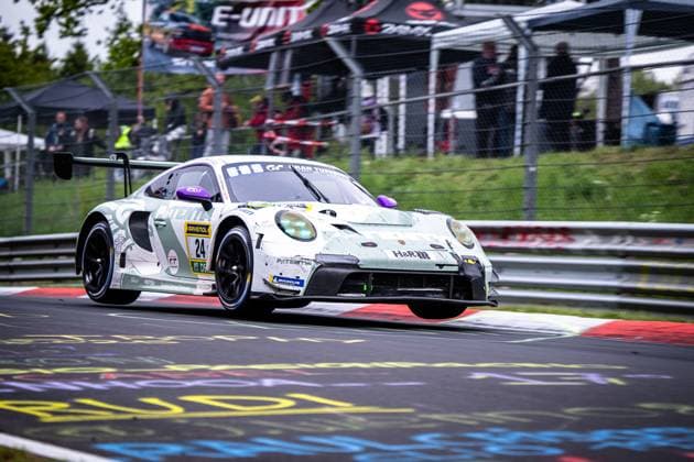 Der Porsche 911 GT3 R Laurens Vanthoor & Laurin Heinrich & Ricardo Feller (Lionspeed GP) von Lionspeed GP nimmt eine Kurve auf der Nordschleife des Nürburgrings. Das weiß-grüne Fahrzeug mit der Startnummer 24 ist mit Sponsoren wie RAVENOL, H&R und Michelin beklebt. Im Hintergrund sind Zuschauer hinter dem Sicherheitszaun zu sehen. Porsche 911 GT3 R 24 von Manthey auf der Nordschleife Copyright: xMichaelxGelhardtx