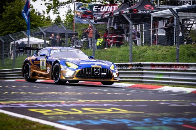 Der Mercedes-AMG GT3 80 von Mercedes-AMG Team RAVENOL durchfährt mit eingeschalteten Scheinwerfern eine Kurve auf der Nordschleife des Nürburgrings. Das Fahrzeug trägt das charakteristische blau-goldene Livery mit RAVENOL- und H&R-Sponsoring und ist im typischen Gran Turismo-Design lackiert. Im Hintergrund verfolgen zahlreiche Zuschauer hinter dem Fangzaun das Renngeschehen. Fabian Schiller & Luca Stolz & Maro Engel & Maxime Martin (Mercedes-AMG Team RAVENOL) Mercedes-AMG GT3 80 von RAVENOL auf der Nordschleife Copyright: xMichaelxGelhardtx