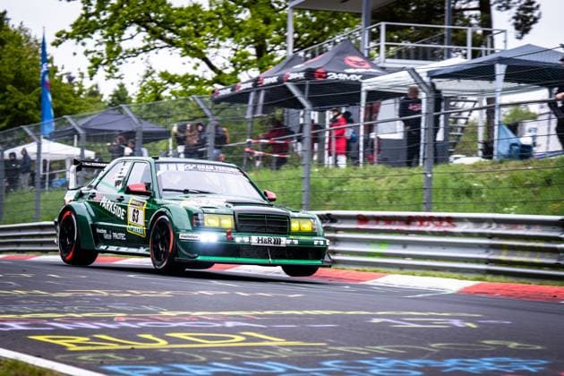 Der dunkelgrüne Mercedes 190E mit der Startnummer 63 von HWA Engineering Speed durchfährt eine Kurve auf dem Nürburgring. Das klassische Tourenwagen-Rennfahrzeug ist mit Sponsoren wie Parkside, H&R und Hankook beklebt und präsentiert sich mit gelben Nebelscheinwerfern sowie einem markanten Heckflügel. Im Hintergrund sind Zuschauer und ein schwarzes Zelt mit dem Aufdruck BAMK zu erkennen. Adam Adelson & James Green & Lance David Arnold & Renger Van der Zande (HWA Engineering Speed) Mercedes 190E 63 von HWA Engineering Speed auf dem Nürburgring Copyright: xMichaelxGelhardtx