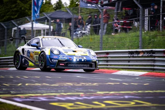 Der Porsche 911 GT3 von Clickversicherung.de TEAM nimmt Kersten Jodexnis & Peter Scharmach & Richard Jodexnis & Richard-Sven Jodexnis & Robin Chrzanowski (Clickversicherung.de TEAM) eine Kurve auf der Nordschleife des Nürburgrings. Das in Blau-Weiß gehaltene Fahrzeug trägt Sponsoren wie RAVENOL, Motul, H&R und OnlineVersicherung.de. Im Hintergrund sind Zuschauer hinter dem Sicherheitszaun zu sehen. Porsche 911 GT3 919 von Clickversicherung.de TEAM auf der Nordschleife Copyright: xMichaelxGelhardtx