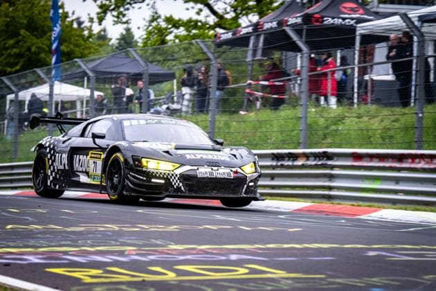 Der Audi R8 LMS GT3 Björn Großmann & Christer Jöns & Otto Blank & Pierre Kaffer (JUTA Racing) von JUTA Racing nimmt eine Kurve auf der Nordschleife des Nürburgrings. Das schwarz-weiß karierte Fahrzeug mit gelben Scheinwerfern trägt die Sponsoren ALPHAZOO, RAVENOL und H&R. Im Hintergrund verfolgen Zuschauer hinter dem Sicherheitszaun das Renngeschehen. Die charakteristischen roten Randsteine der Nordschleife sind gut erkennbar. Audi R8 LMS GT3 71 von JUTA Racing auf der Nordschleife Copyright: xMichaelxGelhardtx