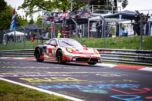 Der Porsche 911 GT3 R von BLACK FALCON Team EAE mit der Startnummer 5 durchfährt eine Kurve auf dem Nürburgring. Das Fahrzeug in der charakteristischen beige-roten Farbgebung mit EAE- und H&R-Sponsoring nimmt die Curbs der rot-weißen Randsteine. Im Hintergrund verfolgen zahlreiche Zuschauer sowie Fotografen hinter dem Zaun das Renngeschehen. Bunte Fanschriften zieren den Asphalt der Nordschleife. Gabriele Piana & Mike Stursberg & Mustafa Mehmet Kaya & Thomas Kiefer (BLACK FALCON Team EAE) Porsche 911 GT3 R 5 von BLACK FALCON Team EAE auf dem Nürburgring Copyright: xMichaelxGelhardtx
