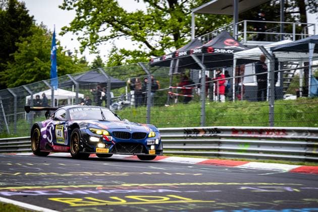 Der BMW Z4 GT3 Frank Nikolaus & Michael Funke & Peter Posavac & Volker Strycek (W.I.S Racing Team powered by Koopman Racing) von W.I.S Racing Team powered by Koopman Racing durchfährt eine Kurve auf der Nordschleife am Nürburgring. Das Fahrzeug in Dunkelblau mit lila Akzenten hat die Scheinwerfer eingeschaltet und zeigt die charakteristischen goldenen Felgen. Sponsoren wie RAVENOL, H&R und Pirelli sind am Fahrzeug erkennbar. Im Hintergrund verfolgen Zuschauer das Rennen hinter dem Fangnetz, ein 24MX-Zelt ist ebenfalls sichtbar. BMW Z4 GT3 40 von W.I.S Racing Team auf der Nordschleife Copyright: xMichaelxGelhardtx