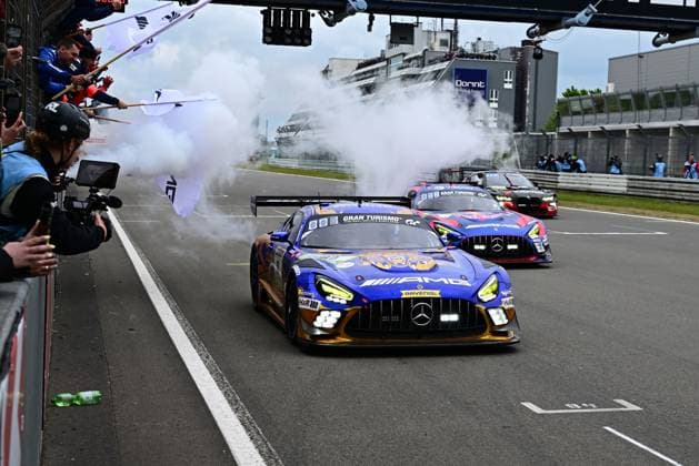 Der Mercedes-AMG GT3 80 von Mercedes-AMG Team RAVENOL fährt durch die Boxengasse des Nürburgring mit aktiviertem Rauchgenerator zur Showfahrt. Das blau-goldene Fahrzeug mit RAVENOL-Branding wird von Zuschauern und Medienvertretern bejubelt, während mehrere weitere GT3-Rennwagen folgen. Mercedes-AMG GT3 80 von Mercedes-AMG Team RAVENOL in der Boxengasse Copyright: xMichaelxGelhardtx