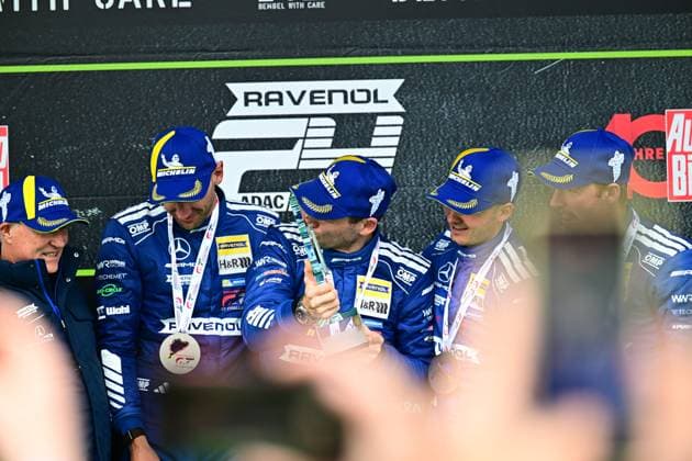 Das siegreiche Team Mercedes-AMG Team RAVENOL mit der Startnummer 80 feiert seinen Sieg auf dem Podium der 24h Nürburgring. Die Fahrer in den charakteristischen blauen Rennoveralls mit Michelin-Helmen und RAVENOL-Branding halten ihre Medaillen und feiern den Langstreckenerfolg. Mercedes-AMG GT3 80 von Mercedes-AMG Team RAVENOL auf dem Podium am Nürburgring Copyright: xMichaelxGelhardtx
