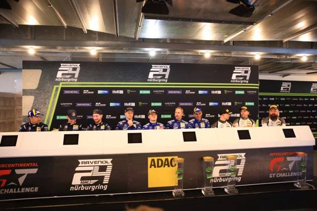 Neun Fahrer sitzen bei einer Pressekonferenz am Nürburgring. Die Aufstellung zeigt Fahrer der Mercedes-AMG Team RAVENOL ( 80) und Red Bull Team ABT ( 84) mit den erkannten Piloten Christian Krognes, Fabian Schiller, Luca Stolz, Maro Engel, Maxime Martin und Mirko Bortolotti. Im Hintergrund sind Sponsoringbanden mit RAVENOL, ADAC, Monster Energy, H&R und weiteren Partnern sichtbar. Fahrerbriefing beim ADAC RAVENOL 24h Nürburgring mit Mercedes-AMG und Red Bull Teams