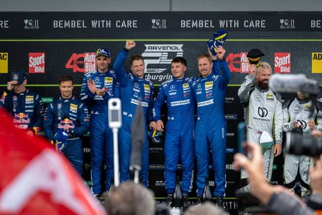 Die Fahrer von Mercedes-AMG Team RAVENOL präsentieren sich auf dem Podium nach ihrem Sieg beim 24-Stunden-Rennen auf dem Nürburgring. Das Team in den charakteristischen blauen Rennanzügen mit RAVENOL-Branding hebt die Trophäe triumphierend in die Luft, während Zuschauer und Fotografen die Siegerehrung dokumentieren. Mercedes-AMG Team RAVENOL 80 feiert Sieg bei 24h Nürburgring 2026 Copyright: xMichaelxGelhardtx
