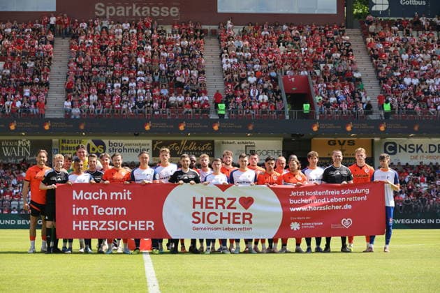 Beide Mannschaften mit dem Banner Herz Sicher - Gemeinsam Leben retten Fussball Landespokal Brandenburgt 2025 2026 Finale FC Energie Cottbus - VfB Krieschow 1921