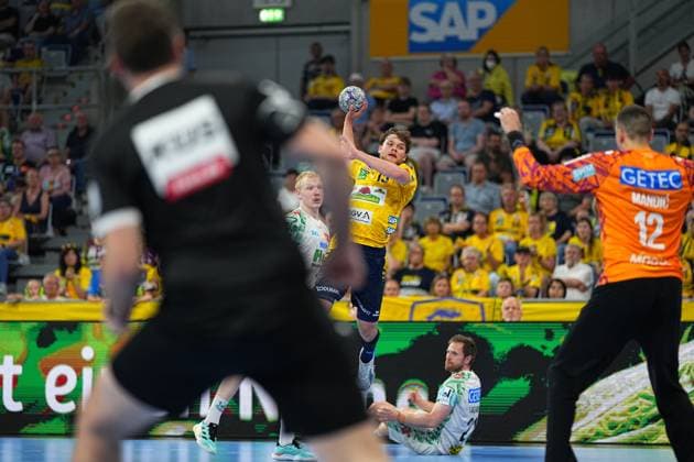 David Möré ( 15; Rhein Neckar Löwen) springt in der SAP Arena hoch und zieht bei einem Gegenstoß zum Wurf ab, während Magdeburg-Torwart Matej Mandi? ( 12) die Arme hochreißt. Magnus Saugstrup ( 23; SC Magdeburg) versucht im Hintergrund den Angriff zu stoppen. David Möré ( 15; Rhein Neckar Löwen) beim Sprungwurf gegen SC Magdeburg