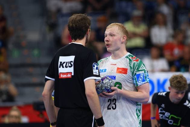 Magnus Saugstrup ( 23, SC Magdeburg) hält den Spielball und spricht mit einem Schiedsrichter in der SAP Arena. Im Hintergrund sind Zuschauer sowie ein weiterer Spieler zu sehen. Magnus Saugstrup ( 23; SC Magdeburg) im Gespräch mit Schiedsrichter