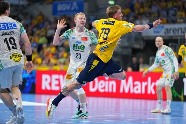 Edwin Aspenbäck ( 78; Rhein Neckar Löwen) springt in gelb-blauem Trikot zum Wurf ab, umgeben von SC-Magdeburg-Spielern in weißen Trikots, darunter Magnus Saugstrup ( 23) und Elvar Örn Jonsson ( 19). Die Szene findet in der vollbesetzten SAP Arena im Rahmen der DAIKIN HBL statt. Edwin Aspenbäck ( 78; Rhein Neckar Löwen) beim Sprungwurf in der SAP Arena