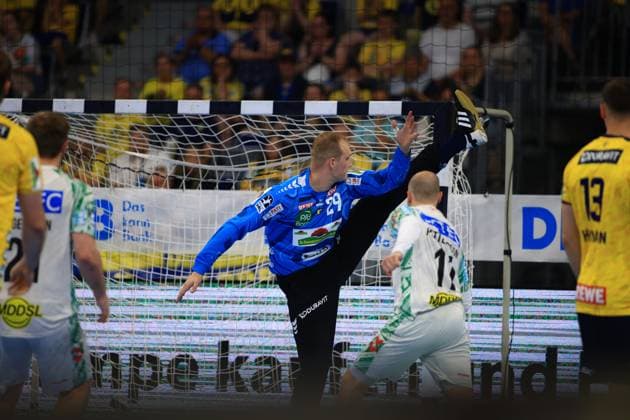 David Späth ( 29; Rhein Neckar Löwen) streckt sich im blauen Torwarttrikot mit einem hohen Beinaufschwung zur Abwehraktion ins Tor der SAP Arena. Im Vordergrund sind Spieler beider Teams zu sehen, darunter ein SC-Magdeburg-Spieler im weißen Trikot sowie Löwen-Spieler 13 Sebastian Heymann im gelben Dress. David Späth ( 29; Rhein Neckar Löwen) bei spektakulärer Parade