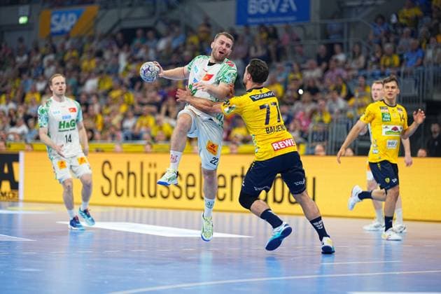 Ein Spieler des SC Magdeburg mit der Trikotnummer 22 springt in der SAP Arena zum Wurf ab und wird dabei von Dani Baijens ( 77, Rhein Neckar Löwen) geblockt. Im Hintergrund sind Omar Ingi Magnusson ( 14, SC Magdeburg) sowie Gino Steenaerts ( 14, Rhein Neckar Löwen) zu sehen. Zweikampf: SC Magdeburg 22 gegen Dani Baijens ( 77; Rhein Neckar Löwen)