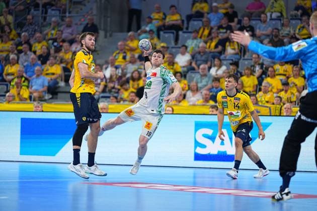 Elvar Örn Jonsson ( 19; SC Magdeburg) springt im weißen Trikot zum Wurf in der SAP Arena, während Steven Plucnar Jacobsen ( 9; Rhein Neckar Löwen) versucht den Abschluss zu blocken. Gino Steenaerts ( 14; Rhein Neckar Löwen) beobachtet die Szene aus dem Hintergrund, rechts im Bild ist der Löwen-Torwart in blauem Trikot zu sehen. Elvar Örn Jonsson ( 19; SC Magdeburg) zieht ab gegen Rhein Neckar Löwen