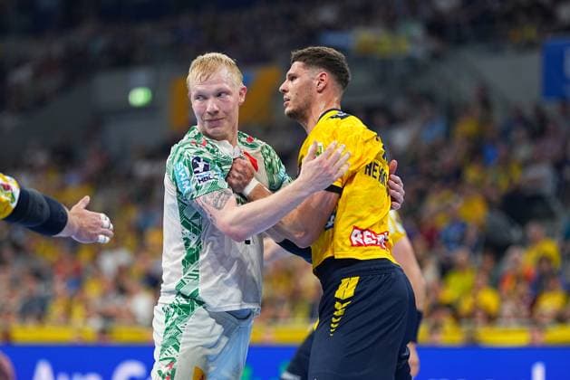 Magnus Saugstrup im weißen SC-Magdeburg-Trikot und Sebastian Heymann im gelben Löwen-Trikot stehen in einem körperbetonten Zweikampf in der SAP Arena. Heymann hält Saugstrup fest, während beide Spieler direkten Körperkontakt haben. Magnus Saugstrup ( 23; SC Magdeburg) im Zweikampf mit Sebastian Heymann ( 13; Rhein Neckar Löwen)