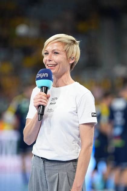 Anett Sattler moderiert mit einem DYN-Mikrofon in der SAP Arena beim DAIKIN HBL-Spiel Rhein Neckar Löwen gegen SC Magdeburg. Sie trägt ein weißes Kempa-Shirt mit DYN-Logo. Moderatorin Anett Sattler mit DYN-Mikrofon in der SAP Arena