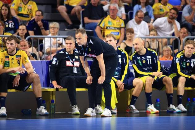 Trainer Maik Machulla beugt sich an der Auswechselbank der Rhein Neckar Löwen nach vorne, neben ihm sitzt Co-Trainer Michel Abt. Auf der Bank sind außerdem Steven Plucnar Jacobsen ( 9) und Lukas Sandell ( 11) zu sehen. Maik Machulla und Michel Abt an der Seitenlinie der Rhein Neckar Löwen