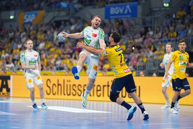 Ein SC-Magdeburg-Spieler im weißen Trikot springt zum Wurf und wird dabei von Dani Baijens ( 77) in gelbem Trikot der Rhein Neckar Löwen geblockt. Gino Steenaerts ( 14; Rhein Neckar Löwen) ist im Hintergrund rechts zu sehen, die SAP Arena ist mit gelb gekleideten Zuschauern gefüllt. SC Magdeburg Spieler ( 23; SC Magdeburg) beim Wurf gegen Dani Baijens ( 77; Rhein Neckar Löwen)
