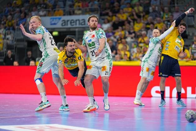 Albin Lagergren ( 21, SC Magdeburg) kämpft in der SAP Arena im Nahkampf gegen einen Löwen-Spieler, während Sebastian Heymann ( 13, Rhein Neckar Löwen) rechts im Bild den Arm ausstreckt. Im Vordergrund ist zudem ein Magdeburg-Spieler mit der Nummer 23 zu sehen, der Ball liegt am rechten Bildrand auf dem Boden. Albin Lagergren ( 21; SC Magdeburg) im Zweikampf gegen Sebastian Heymann ( 13; Rhein Neckar Löwen)
