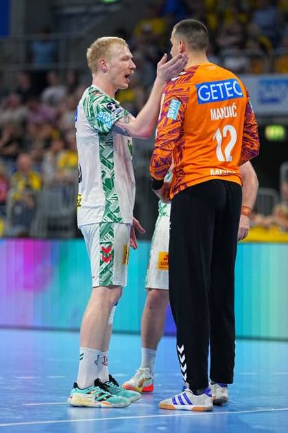 Magnus Saugstrup im weißen SC-Magdeburg-Trikot spricht mit Torwart Matej Mandi? ( 12) im orangenen Torwarttrikot auf dem Spielfeld der SAP Arena. Saugstrup legt dabei eine Hand an Mandi?s Hals, während beide miteinander kommunizieren. Magnus Saugstrup ( 23; SC Magdeburg) im Gespräch mit Matej Mandi? ( 12; SC Magdeburg)