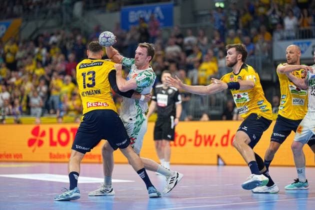 Sebastian Heymann ( 13; Rhein Neckar Löwen) stellt einen weißgekleideten SC Magdeburg Spieler im Angriff, der den Ball über den Kopf hebt. Im Hintergrund sind Lukas Sandell und Steven Plucnar Jacobsen (beide Rhein Neckar Löwen) in der Abwehrformation zu sehen. Sebastian Heymann ( 13; Rhein Neckar Löwen) blockt SC Magdeburg Angreifer