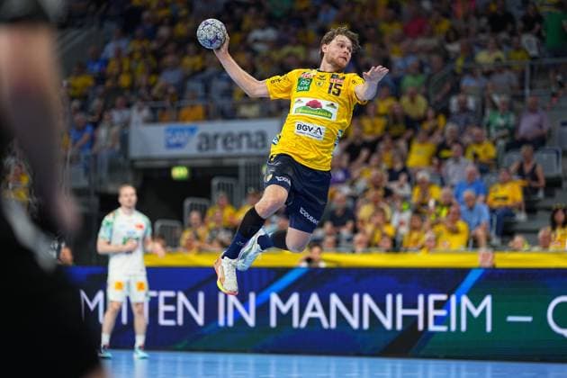 David Möré ( 15) von den Rhein Neckar Löwen springt hoch in die Luft und zieht zum Wurf ab, den Ball in der erhobenen Wurfhand. Im Hintergrund ist ein Spieler in weißem Trikot (SC Magdeburg) zu sehen, die SAP Arena ist mit gelb gekleideten Fans gefüllt. David Möré ( 15; Rhein Neckar Löwen) beim Sprungwurf