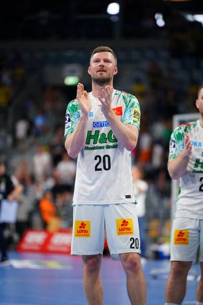 Philipp Weber ( 20; SC Magdeburg) klatscht nach dem Spiel in der SAP Arena in die Hände. Im weißen Trikot mit grünem Muster steht er auf dem Spielfeld und blickt nach oben. Philipp Weber ( 20; SC Magdeburg) applaudiert in der SAP Arena