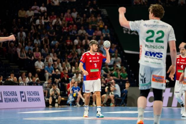 Jacob Lassen vom HSV Hamburg hält den Ball in der rechten Hand während eines Spielzugs in der Barclays Arena. Im Hintergrund sind Spieler von Frisch Auf Göppingen in weißen Trikots sichtbar, darunter Erik Persson ( 22) mit erhobener Hand. Jacob Lassen ( 9; HSV Hamburg) mit Ball in der Barclays Arena Copyright: xPhilippHeistx