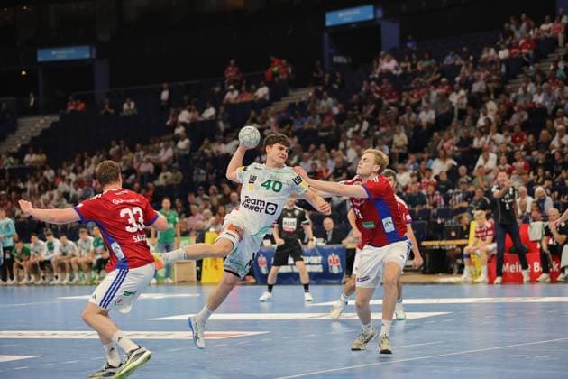 Elias Newel von Frisch Auf Göppingen springt mit dem Ball in der rechten Hand zum Wurf ab, während zwei Hamburger Abwehrspieler versuchen, den Wurf zu blocken. Die Barclays Arena ist vollbesetzt und schafft eine intensive Spielatmosphäre. Elias Newel ( 40; Frisch Auf Göppingen) beim Sprungwurf gegen HSV Hamburg