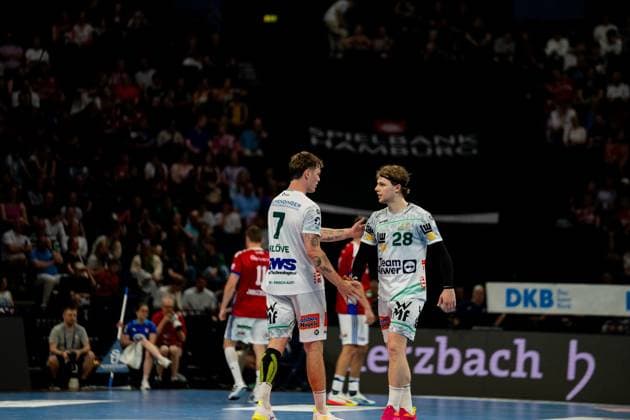 Zwei Spieler von Frisch Auf Göppingen in weißen Trikots unterhalten sich während einer Spielunterbrechung in der Barclays Arena. Im Hintergrund sind Zuschauer und HSV-Hamburg-Spieler in roten Trikots zu sehen. Handball Verein Hamburg vs. Frisch Auf Göppingen Copyright: xPhilippHeistx