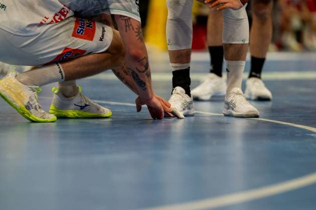 Detailaufnahme von Spielern beider Mannschaften während einer intensiven Spielszene auf dem Handballfeld. Die Aufnahme zeigt die unteren Körperpartien mehrerer Spieler in weißen Trikots von Frisch Auf Göppingen und weiteren Spielern, wobei eine Hand eines Spielers den Ball am Boden berührt. Handball Verein Hamburg vs. Frisch Auf Göppingen Copyright: xPhilippHeistx