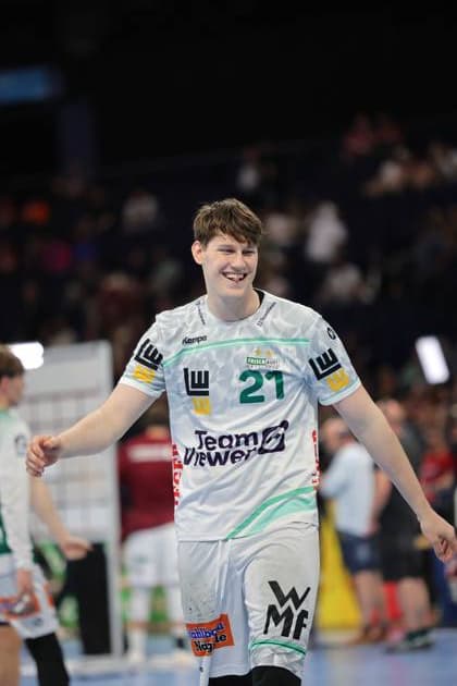 Sascha Brodbeck trägt das weiße Heimtrikot von Frisch Auf Göppingen mit der Nummer 21 und lächelt während eines Spiels in der Barclays Arena. Der Spieler bewegt sich entspannt über das Spielfeld. Sascha Brodbeck ( 21; Frisch Auf Göppingen) lächelnd in der Barclays Arena