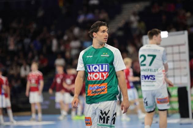 Spieler in grünem Trikot mit weißen Ärmeln von Frisch Auf Göppingen steht während einer Spielunterbrechung auf dem Spielfeld der Barclays Arena. Im Hintergrund sind weitere Spieler und Zuschauer in der Halle sichtbar. Oskar Sunnefeldt ( 27; Frisch Auf Göppingen) während Spielunterbrechung