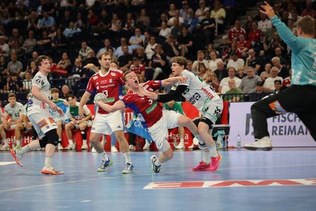 Erik Persson ( 22; Frisch Auf Göppingen) in weißem Trikot wird von Niklas Weller ( 13; HSV Hamburg) und Moritz Sauter ( 33; HSV Hamburg) in rotem Trikot abgewehrt. Die Szene zeigt einen intensiven Zweikampf in der Barclays Arena mit Zuschauern im Hintergrund. Erik Persson ( 22; Frisch Auf Göppingen) im Zweikampf gegen Niklas Weller und Moritz Sauter