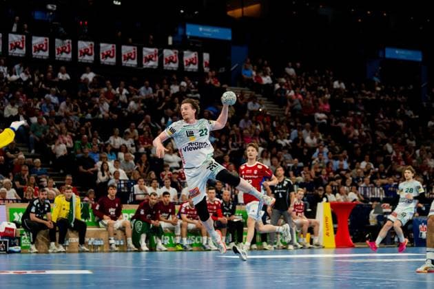 Erik Persson springt zum Torwurf ab und hält den Ball in der Luft. Im Hintergrund sind Zuschauer der Barclays Arena und Spieler beider Mannschaften zu sehen. Handball Verein Hamburg vs. Frisch Auf Göppingen Copyright: xPhilippHeistx